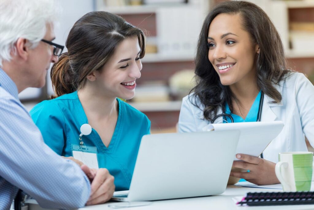 Nurse smiling at laptop with doctor reviewing documentation