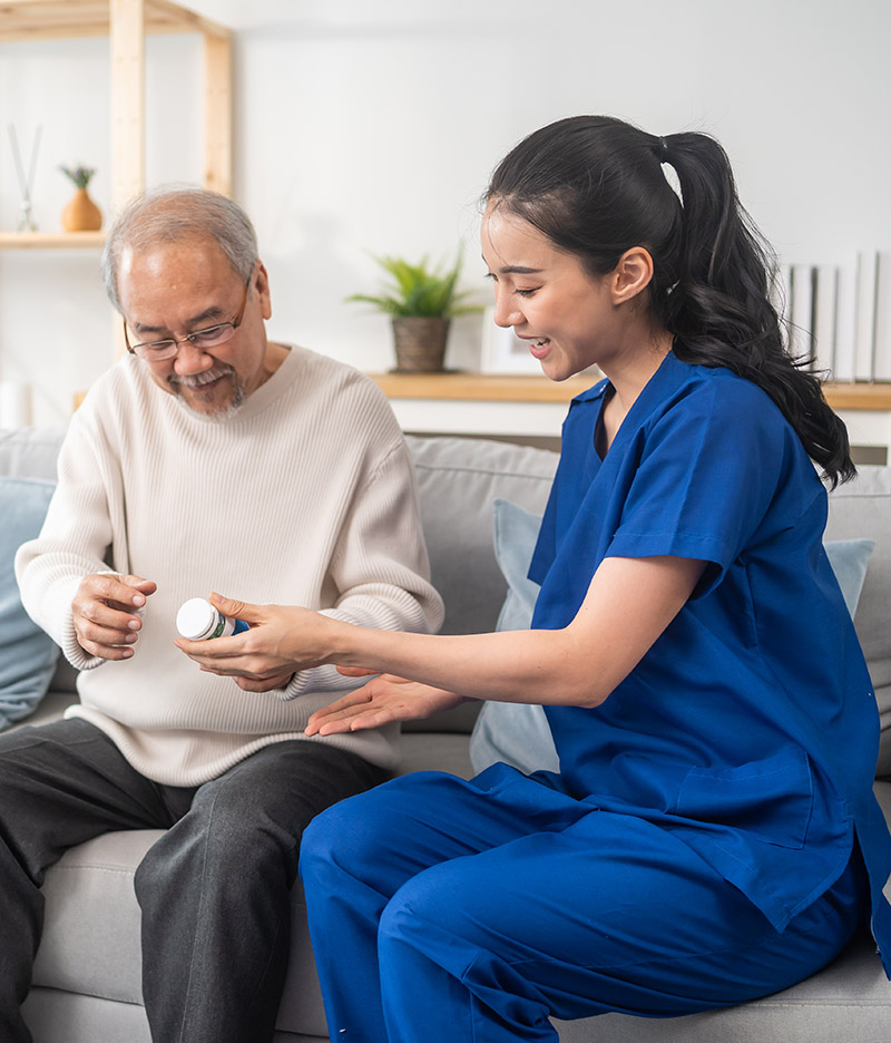 Female pharmacist holding medicine pills bottle, explaining prescription to elderly man in long-term care room